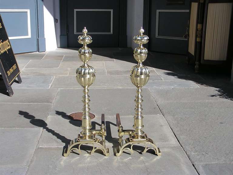 Pair of Italian brass andirons with faceted ball tops, figural finial faces, turned bulbous plinths, matching finial log stops, and terminating on scrolled feet. Early 19th Century