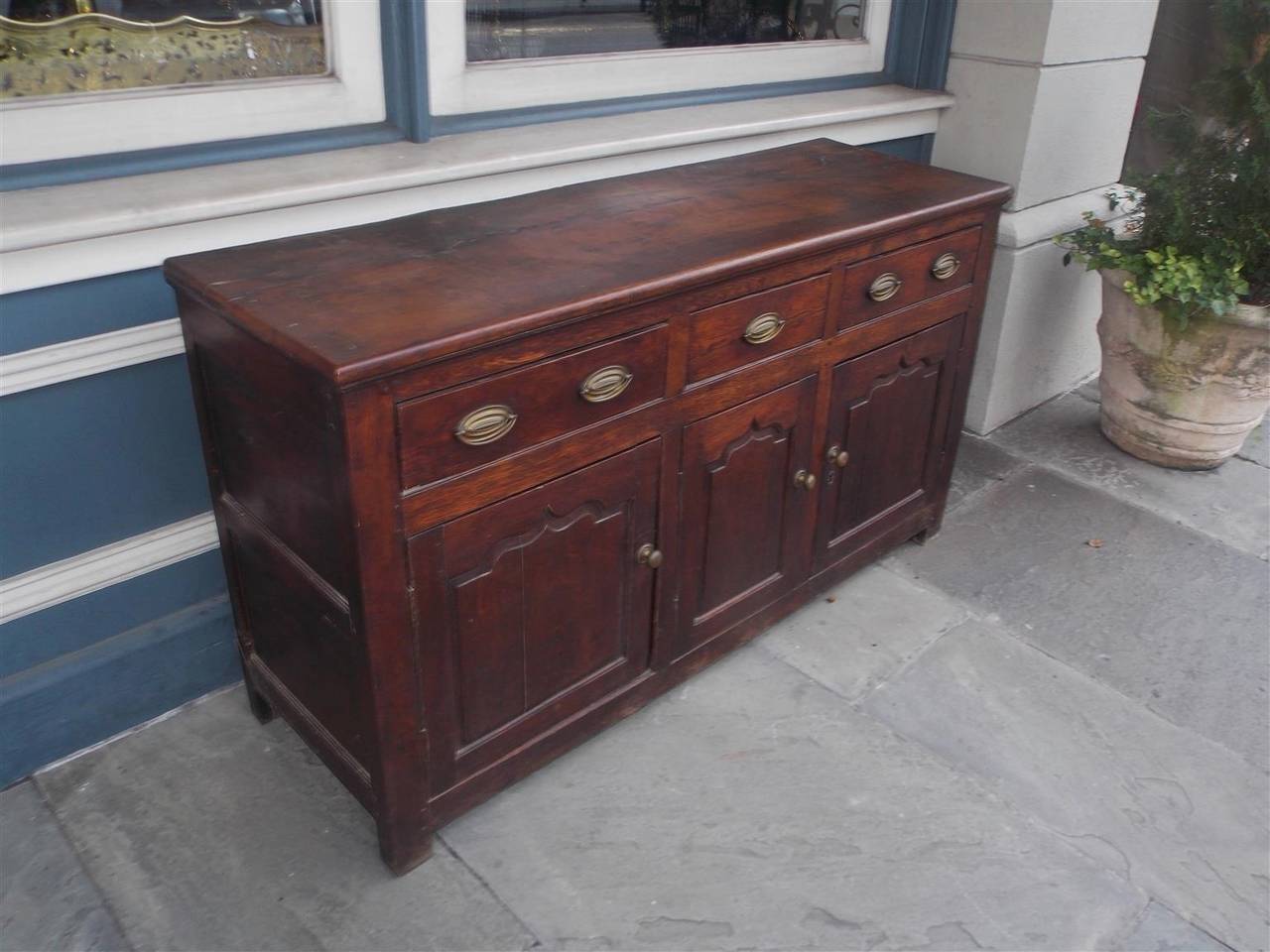 English oak three-drawer credenza with oval period brasses, three lower case cabinet doors and terminating on original block feet, Late 18th Century.