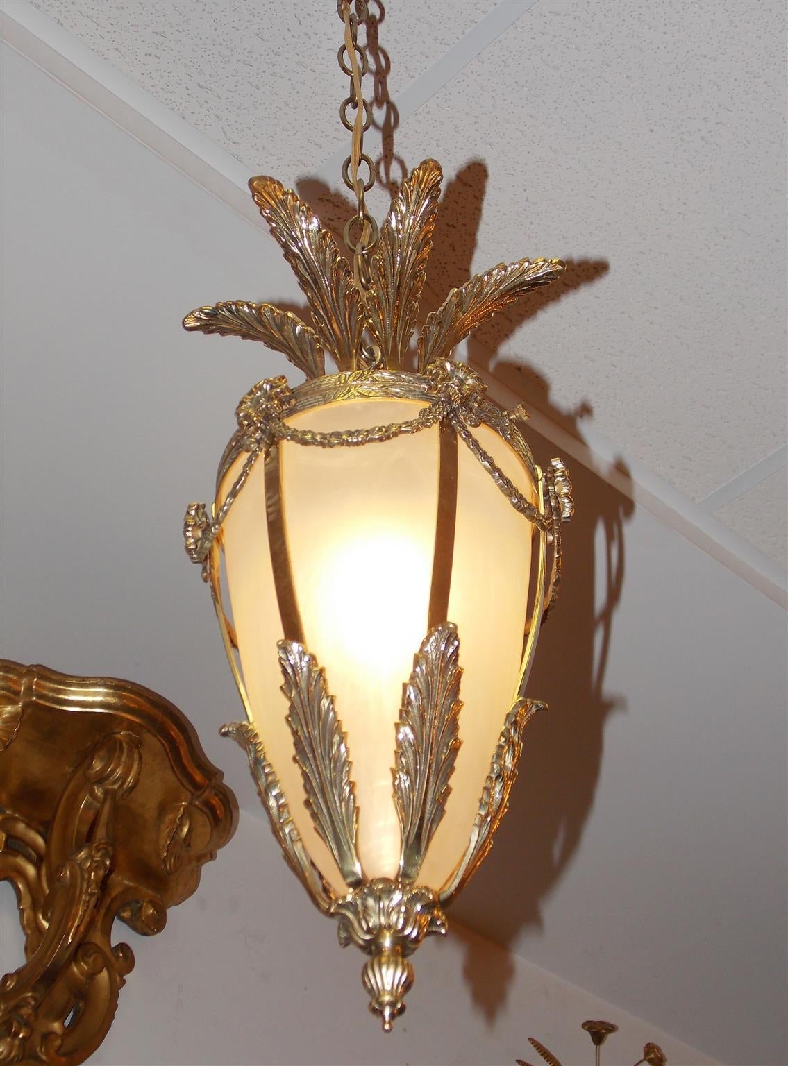 French brass hanging lantern with acanthus leaf motif, floral bell flower swags and medallions, original frosted globe and terminating with a fluted bulbous finial. Originally gas and has been electrified, Mid-19th century.