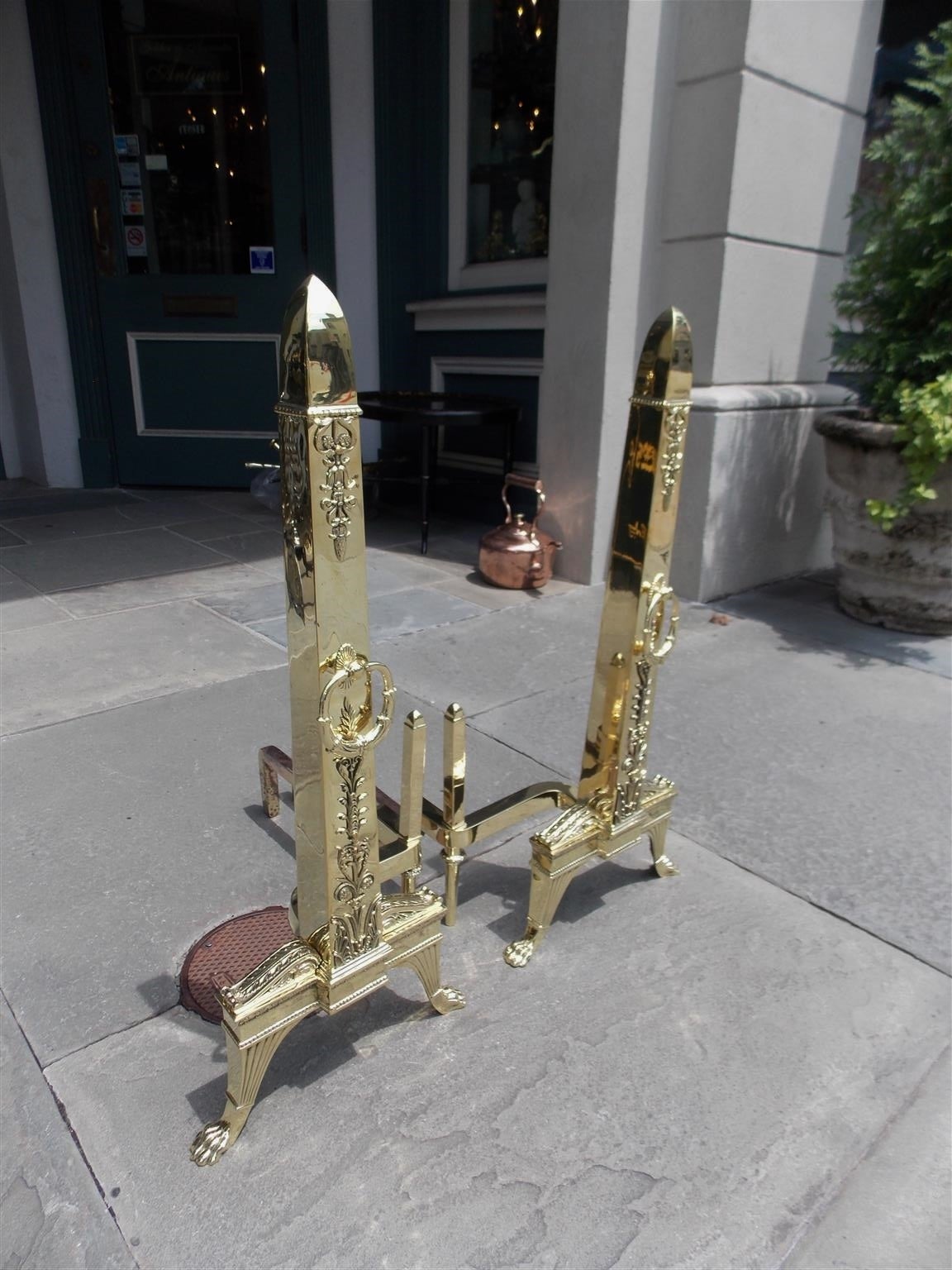 Pair of Monumental French brass obelisk andirons with decorative bead work, floral filigree, centered decorative rings, matching log stops, and terminating on acanthus scrolled fluted legs with lions paw feet.  Early 19th Century