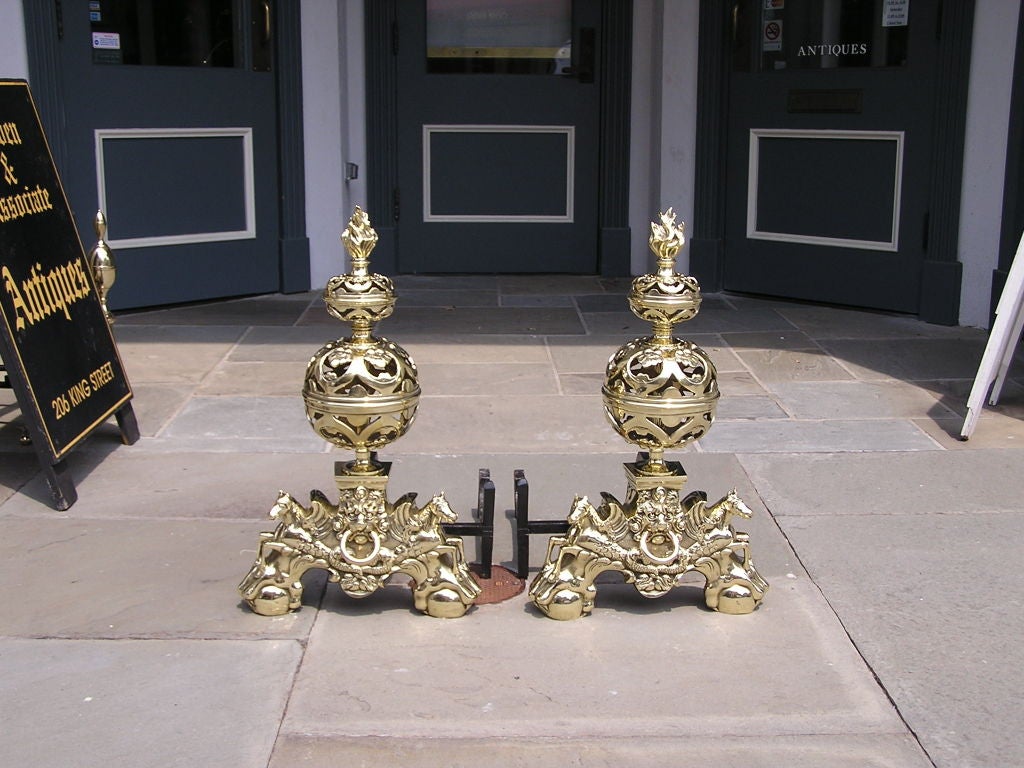 Pair of English brass andirons with flame finials , chased pierced ball tops , flanking sea horses , lions head with centered ring , and terminating on ball and claw feet. Early 19th Century