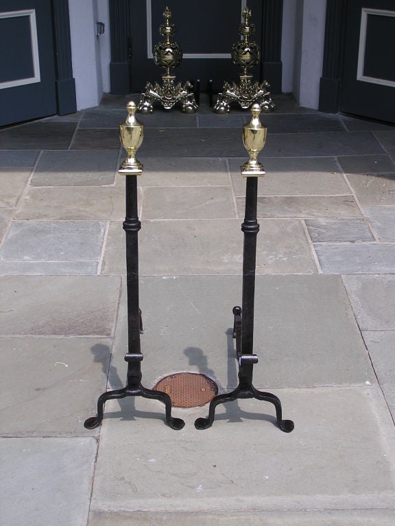 Pair of American wrought iron andirons with brass urn finial tops, scrolled decorative spit hook , and terminating on penny feet. Columns of andirons were originally used for axle's on a horse drawn carriage. Late 18th Century