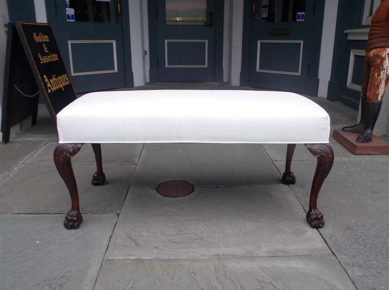 English mahogany upholstered bench with carved acanthus knee and terminating on tapered legs with hairy paw feet. Bench is covered in white muslin. Mid 19th century