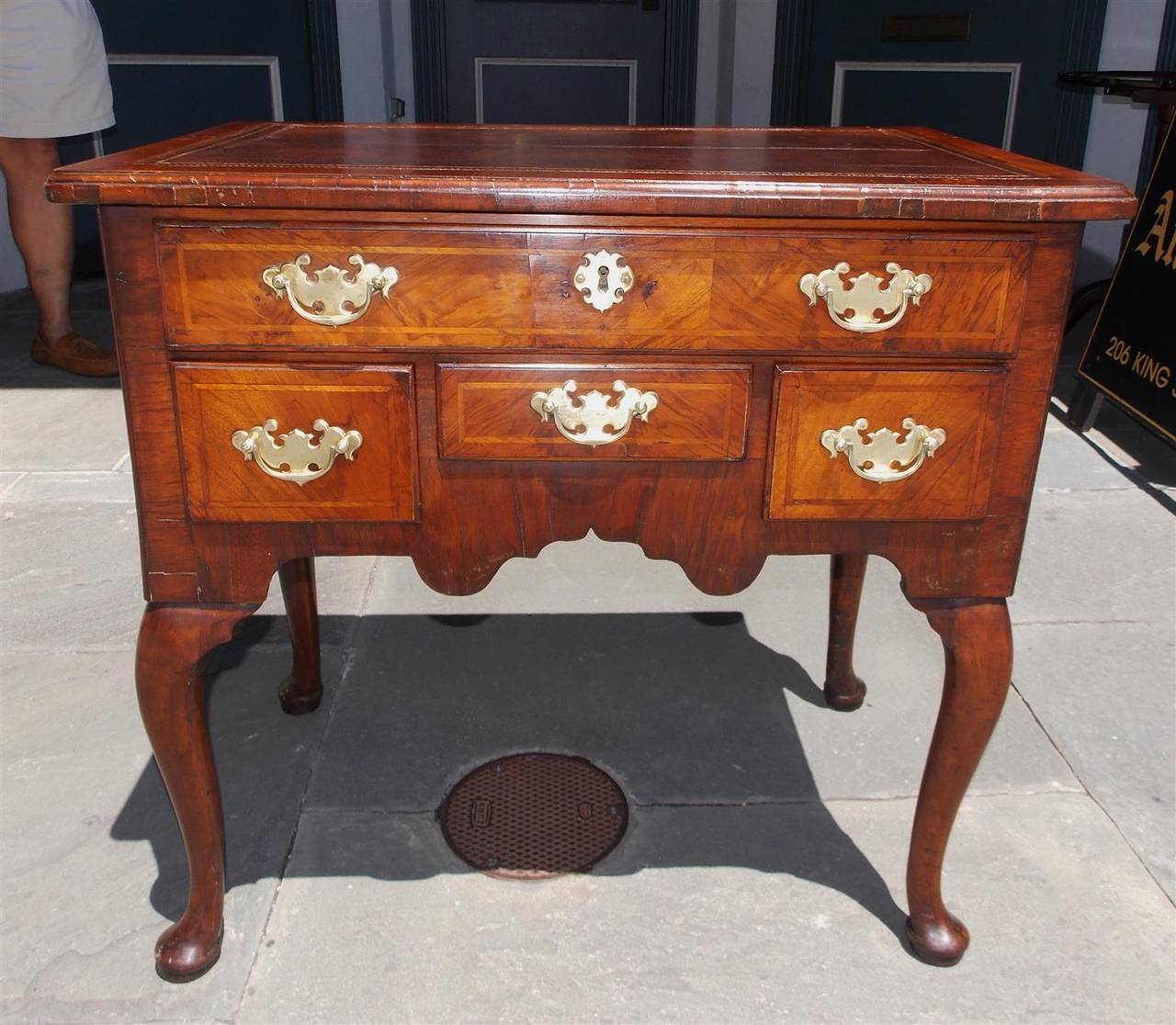 English Queen Anne burl walnut low boy with original leather top, inlaid feather banding, original brasses, carved skirt and terminating on carved knees with pad feet, Mid-18th Century.