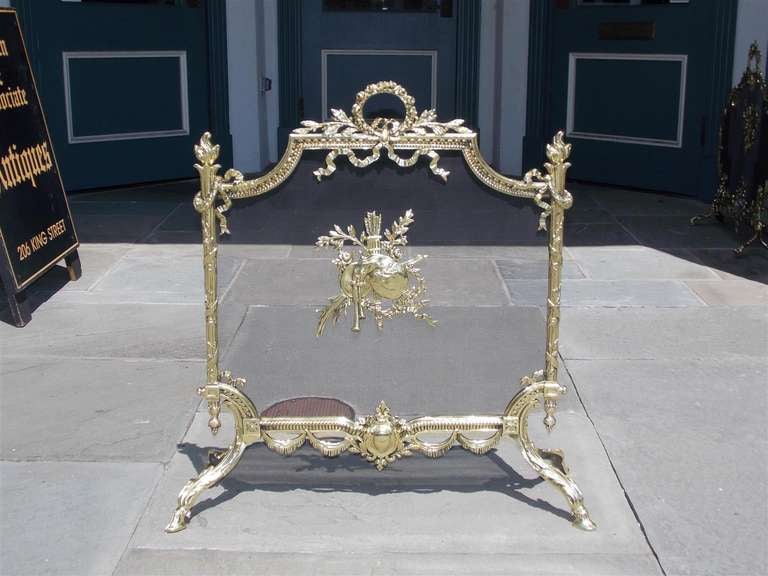 French brass free standing firescreen with centered decorative laurel wreath ribbon motif, flanking flame finials, floral swags, and terminating on acanthus legs with hoof feet.  Dealers please call trade price.