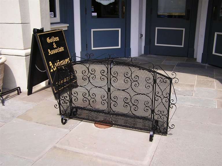 American wrought iron two panel freestanding fire screen with decorative scroll work, wire mesh, hinged doors, and terminating on scrolled legs.  Mid-19th Century