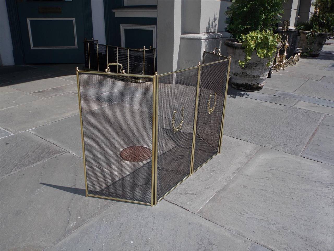 Parafuoco francese pieghevole a quattro pannelli in ottone con maniglie in ottone e supporti decorativi a corona d'alloro.  Ogni pannello è alto 24,25