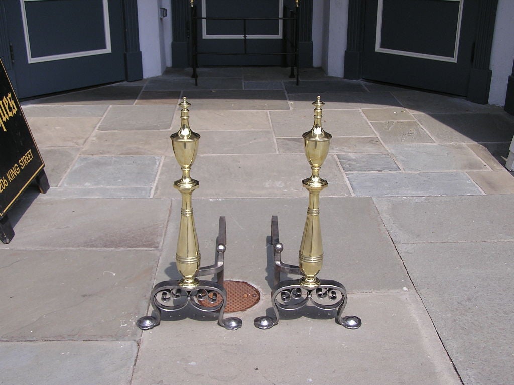 Pair of American brass and polished steel andirons with urn finial top,hand chased beading, scrolled legs with penny feet and hand hammered log stops.