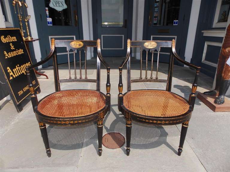 Pair of English Regency stenciled and gilt armchairs with classical painted oval scenes, cane seats, and terminating on turned stenciled bulbous legs, late 18th Century.