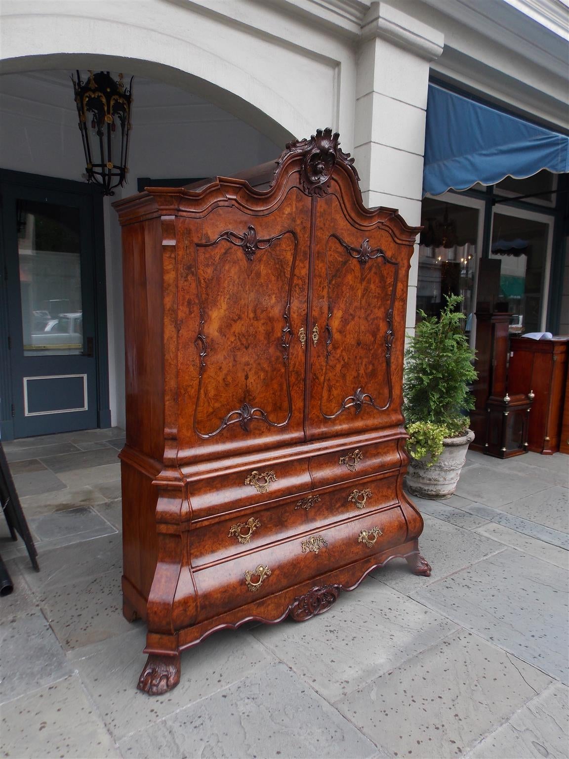 Dutch Chippendale burl walnut bombay graduated three-drawer linen press with serpentine carved floral cartouche, flanking foliage hinged doors, original floral brasses, interior shelving with three drawers, serpentine carved foliage skirt, and