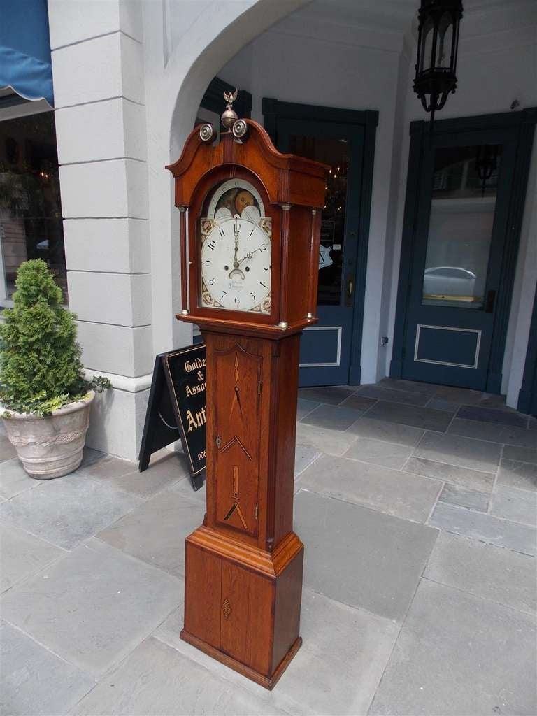 English Oak Masonic tall case clock with brass Eagle finial over broken pediment, arched bonnet, fluted brass hood columns with upper secret drawer, hand painted decorative face, masonic inlaid symbols, terminating on squared plinth with reeded
