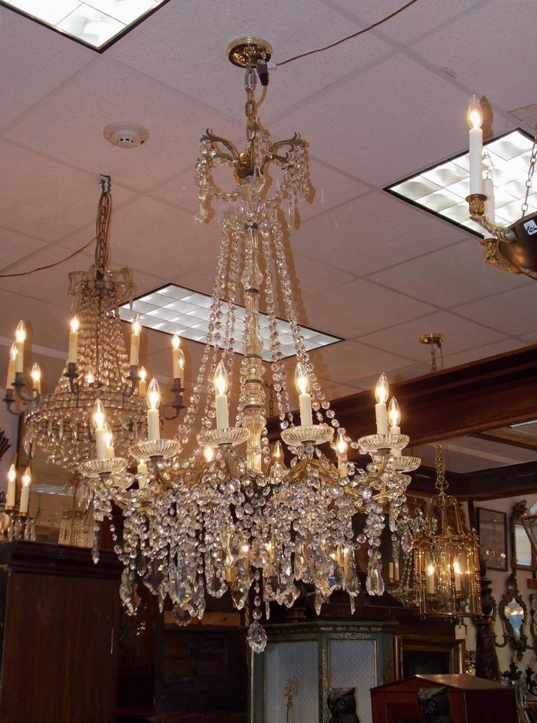 French gilt bronze and crystal twelve light chandelier with crystal fluted centered column, scrolled floral decorative arms, and completed with faceted crystals. Originally candle powered and has been electrified. Early 19th Century.