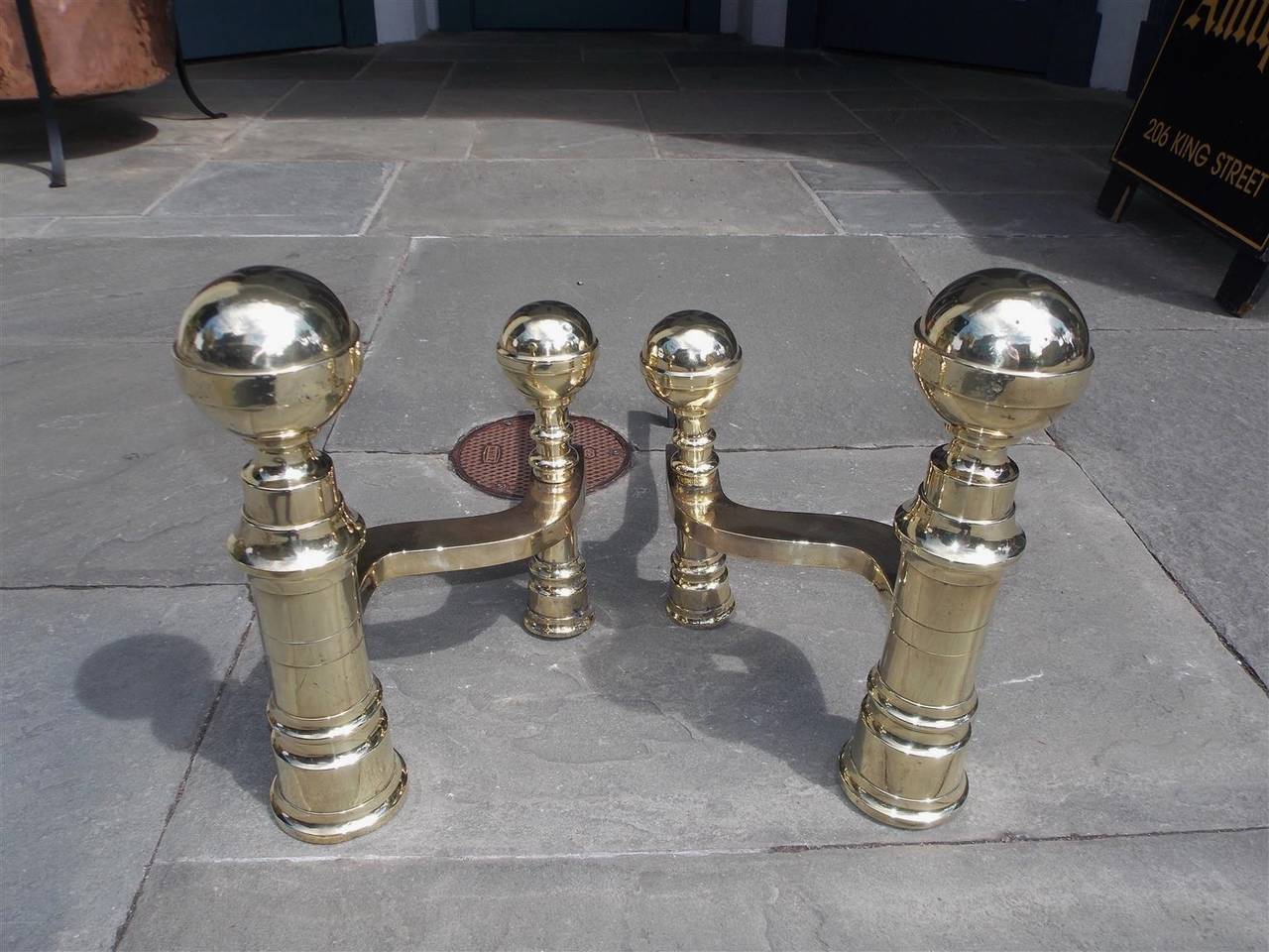 Pair of American brass ball top andirons with turned bulbous ring plinths, matching log stops, and original wrought iron dog legs, Early 19th century.
