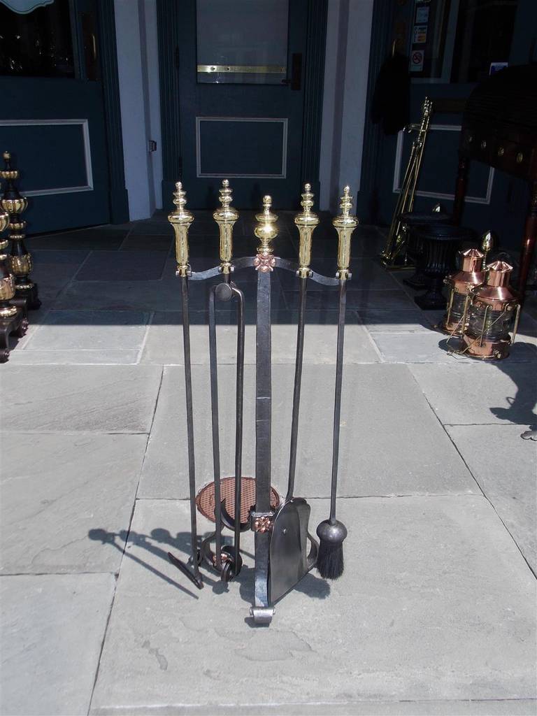 Set of American wrought iron and brass finial fire tools on stand with copper medallions, tapered squared column, terminating on scrolled tripod legs. Set consist of poker, tong, shovel, and brush.  Early 19th Century.