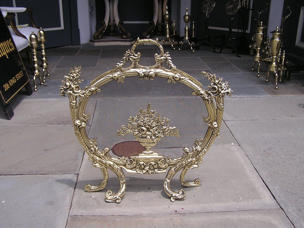 French brass fire screen with centered floral urn, flanked by floral baskets, top centered floral handle, and ending on scrolled floral feet.