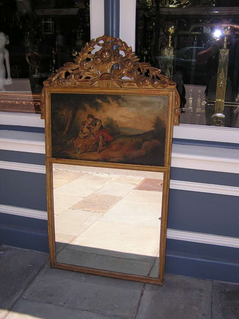 French gilt wood and gesso trumeau wall mirror with a central carved fruit floral basket, flanking tassel borders, interior bead work, and painted oil on canvas figural landscape. Mirror retains the original glass and wood backing. Signed on