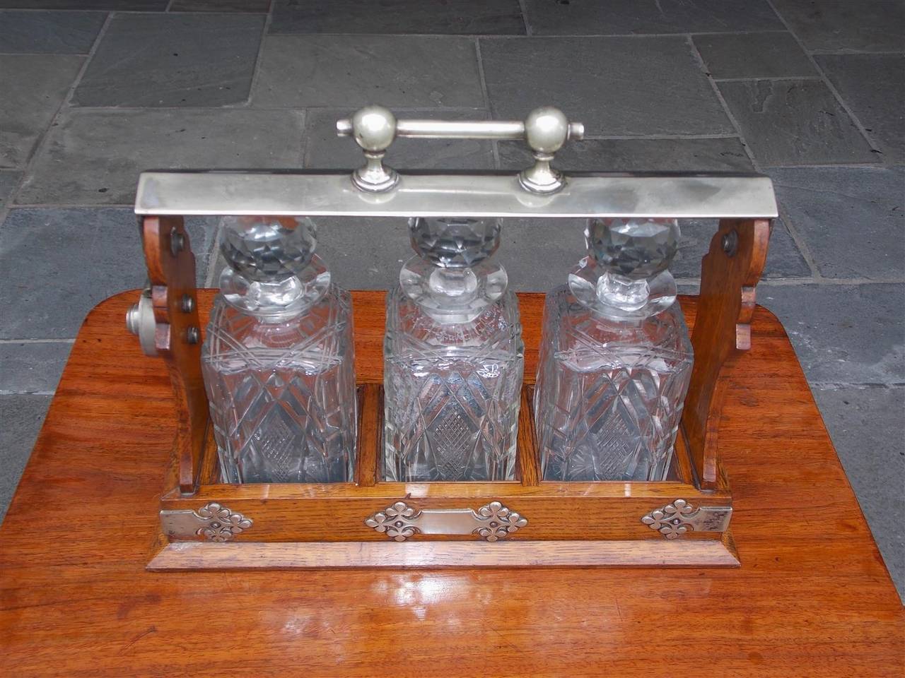 English Oak Tantalus with original ball faceted swivel locking handle, Nickel silver side mounts, original three cut crystal decanters with stoppers, and resting on a raised rectangular molded edge base. Stamped by maker. Birmingham Daniel & Arter.