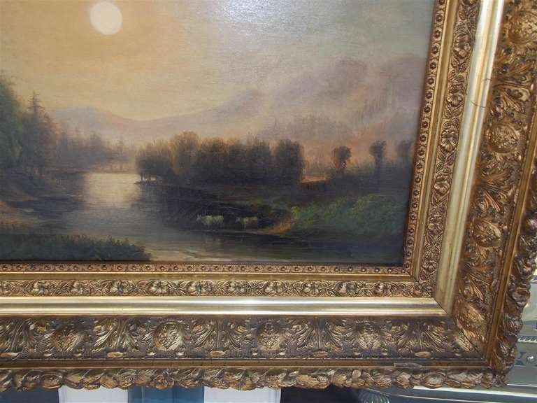 Paesaggio americano ad olio su tela con un ruscello che scorre, alberi e montagne, mucche che si abbeverano in primo piano, sole sullo sfondo, racchiuso nelle barelle originali e nella cornice originale floreale intagliata e dorata. Metà del XIX