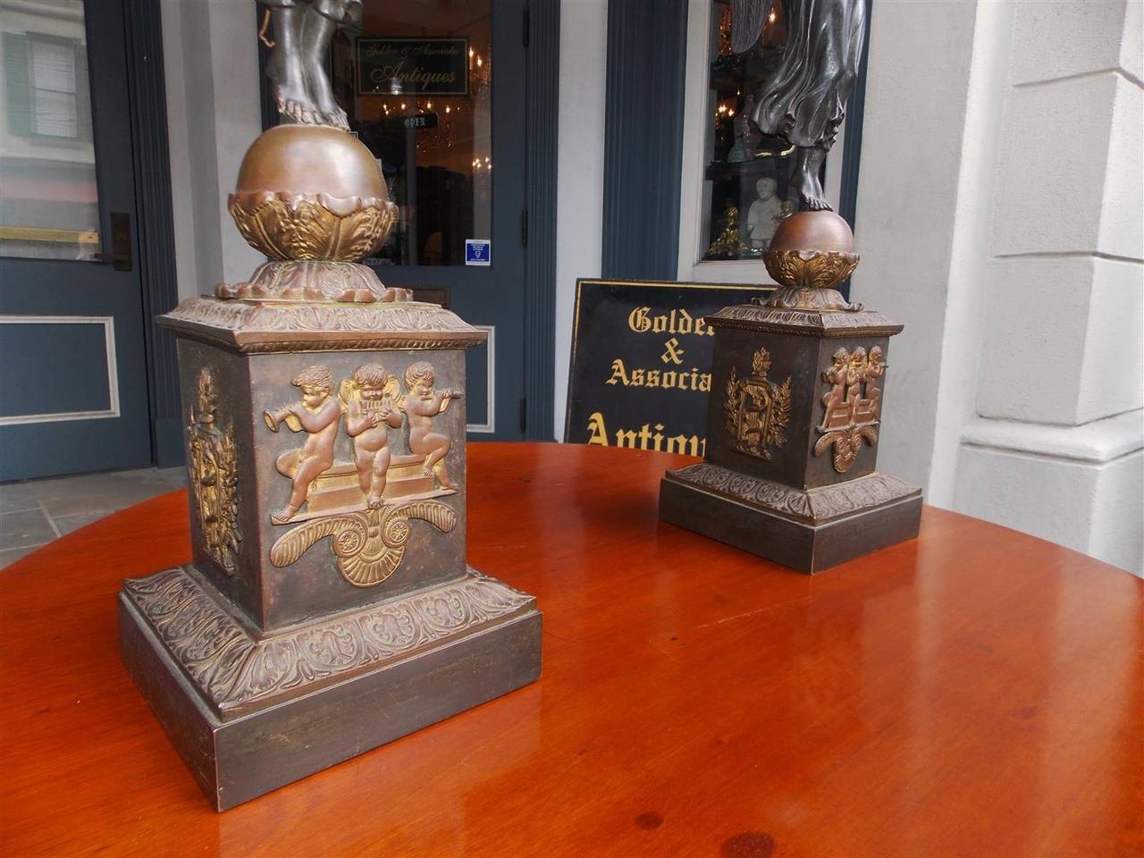 Ein Paar französischer Kandelaber aus vergoldeter Bronze und bemalt mit fünf verschnörkelten, floralen Akanthusarmen, geschmückt mit flankierenden Engelsfiguren, die auf runden Kugeln über quadratischen Sockeln mit Cherub- und Filigranmotiven
