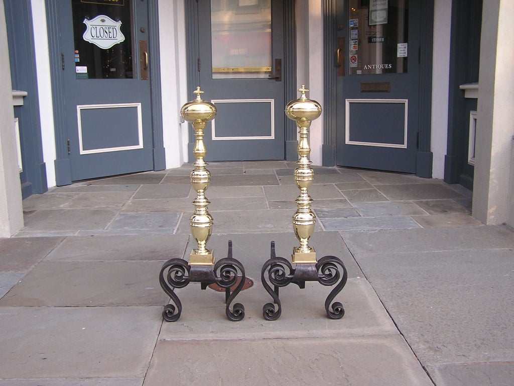 Pair of English brass and wrought iron ball top andirons with turned bulbous shaft, and ending on scrolled iron feet.
