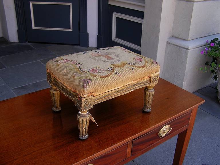Italian gilt wood needlepoint foot stool with carved corner floral medallions, articulated carved skirt, and terminating on bulbous fluted ringed legs.  Early 19th Century.