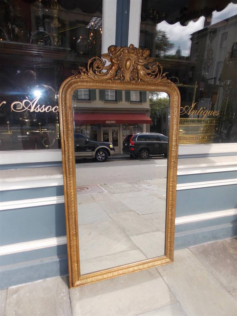 French gilt carved wood wall mirror with centered crest medallion, flanking cherubs perched on acanthus carved scrolled decorative work and molded foliage border.  Mirror retains the original glass and wood backing.  Late 18th Century