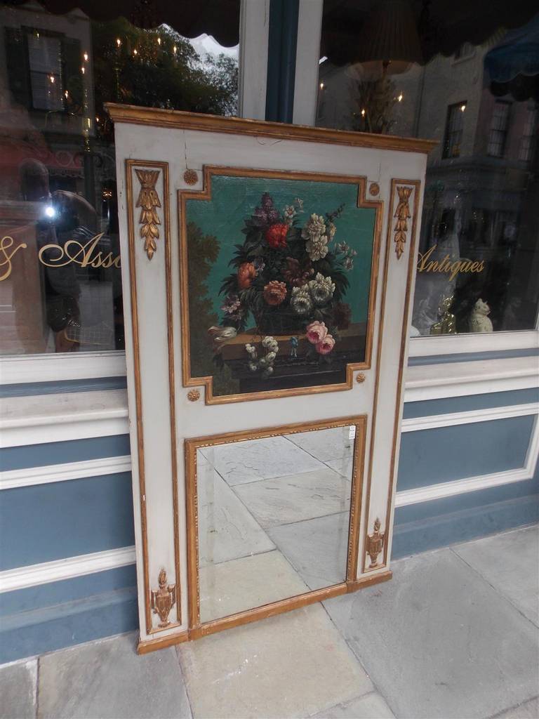 French painted and gilt trumeau mirror with original oil on canvas floral basket, graduated carved corner foliage, floral medallions, and lower flanking flamed urns.  Mirror retains the original glass and wood backing. Late 18th Century