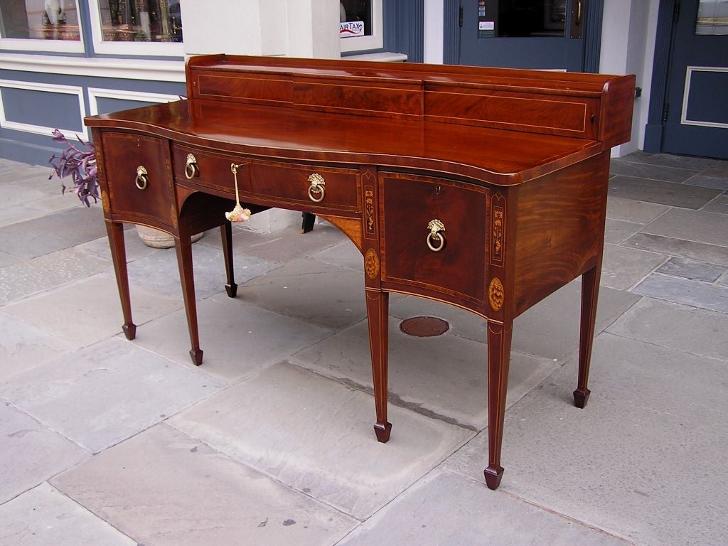 English Hepplewhite serpentine mahogany stage top sideboard with satinwood shell , urn , and floral motif inlays . Sideboard is cross banded in mahogany and has the original floral brasses terminating on tapered legs with spade feet. Late 18th