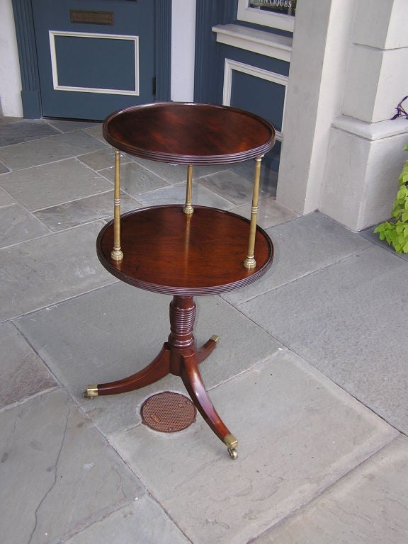 American mahogany two tiered  supper table with brass decorative column supports, reeded and turned tripod pedestal, and terminating on original brass casters. Early 19th Century