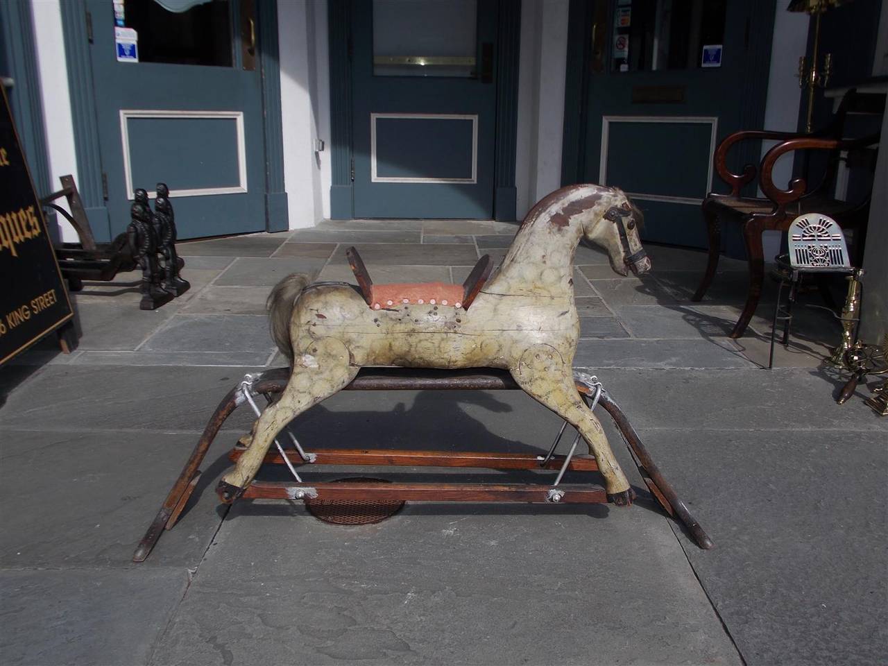American carved wood and faux painted child's rocking horse with cloth saddle, original horse hair, and resting on wood base with stretchers.  Late 19th Century.