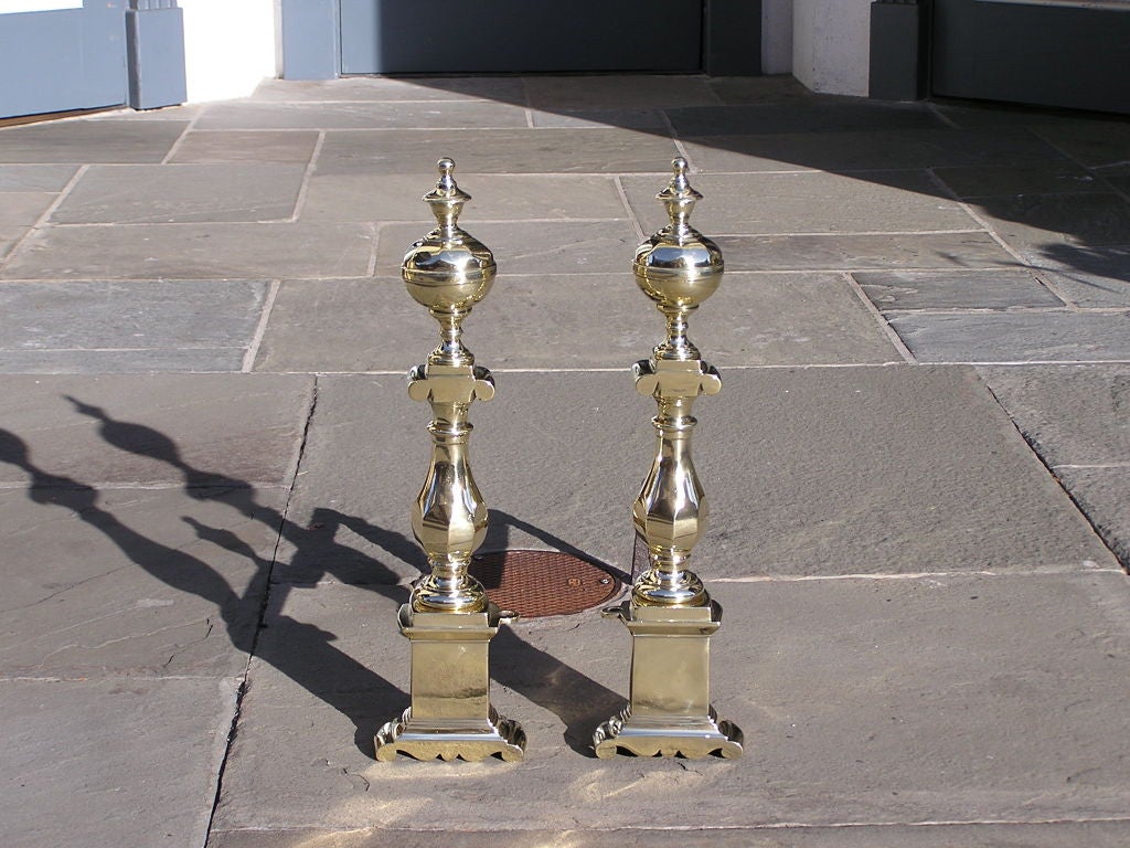 Pair of Charleston brass andirons with faceted finial ball top, bulbous centered column,matching finial log stops, and ending on square & scroll plinths.
