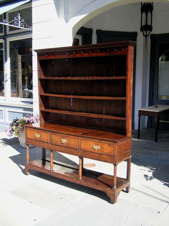 English Chippendale oak welsh dresser with carved reeded cornice, three interior shelves, original wrought iron hooks, three centered drawers supported by turned columns with a lower shelf, winged brasses, and resting on the original blocked bracket