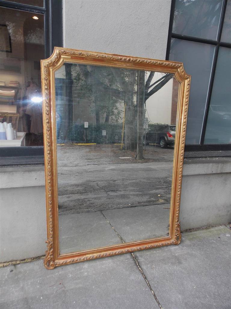 French gilt carved wood and gesso wall mirror with flanking cut corners, ribbon and floral molded edge, single row of beading, and resting on acanthus carved floral motif. Mirror retains the original glass and wood backing. Early 19th Century.