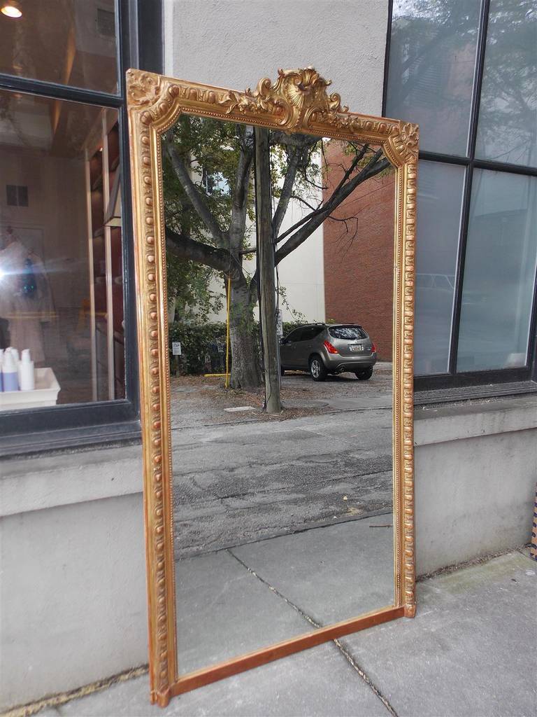 French gilt carved wood and red lacquer floral crest wall mirror with flanking cut corners, egg and dart molded edge, and interior single row of beading. Mirror retains the original glass. Early 19th century.