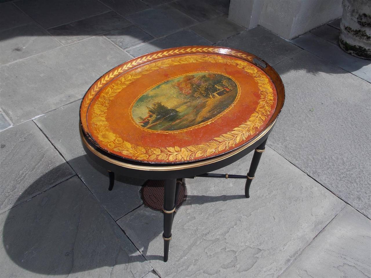 English tole landscape oval tray with floral borders, two side handles, and resting on painted and gilt faux bamboo splayed leg stand. Stand was made at later date, Early 19th century.