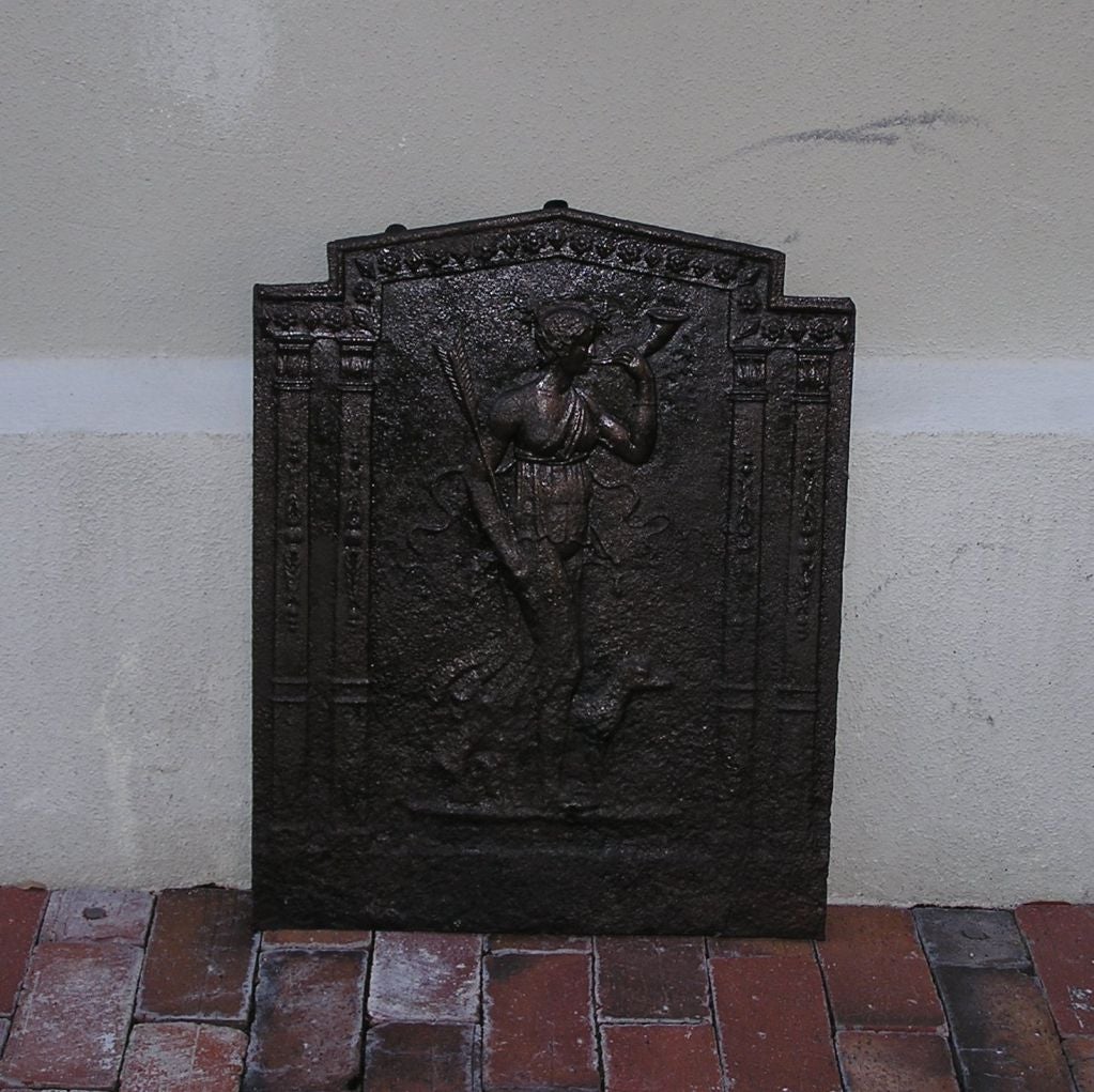 Plaque de cheminée en fonte anglaise avec figure mythologique d'Eros et son compagnon canin, bordure en médaillon,  et flanquée de colonnes florales verticales. Fin du 18e siècle
