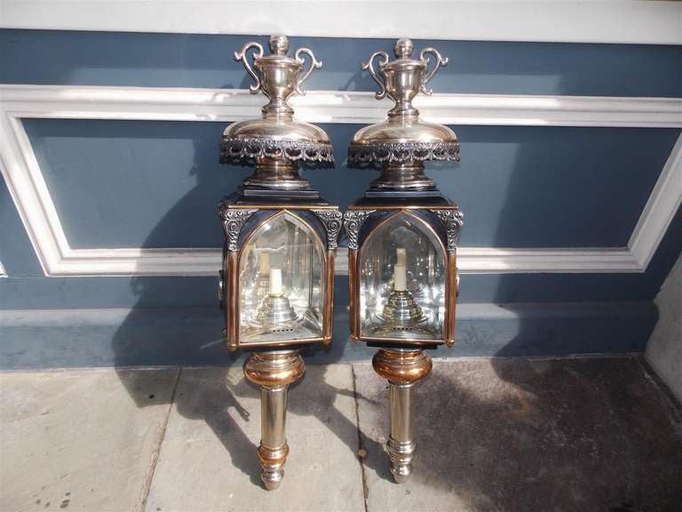 Pair of American nickel silver over copper & brass coach lanterns with urn finials,  floral swag motif, and terminating on a turned bulbous reservoir. Coach lanterns have the original beveled glass & brass mounting brackets attached . Pair have been
