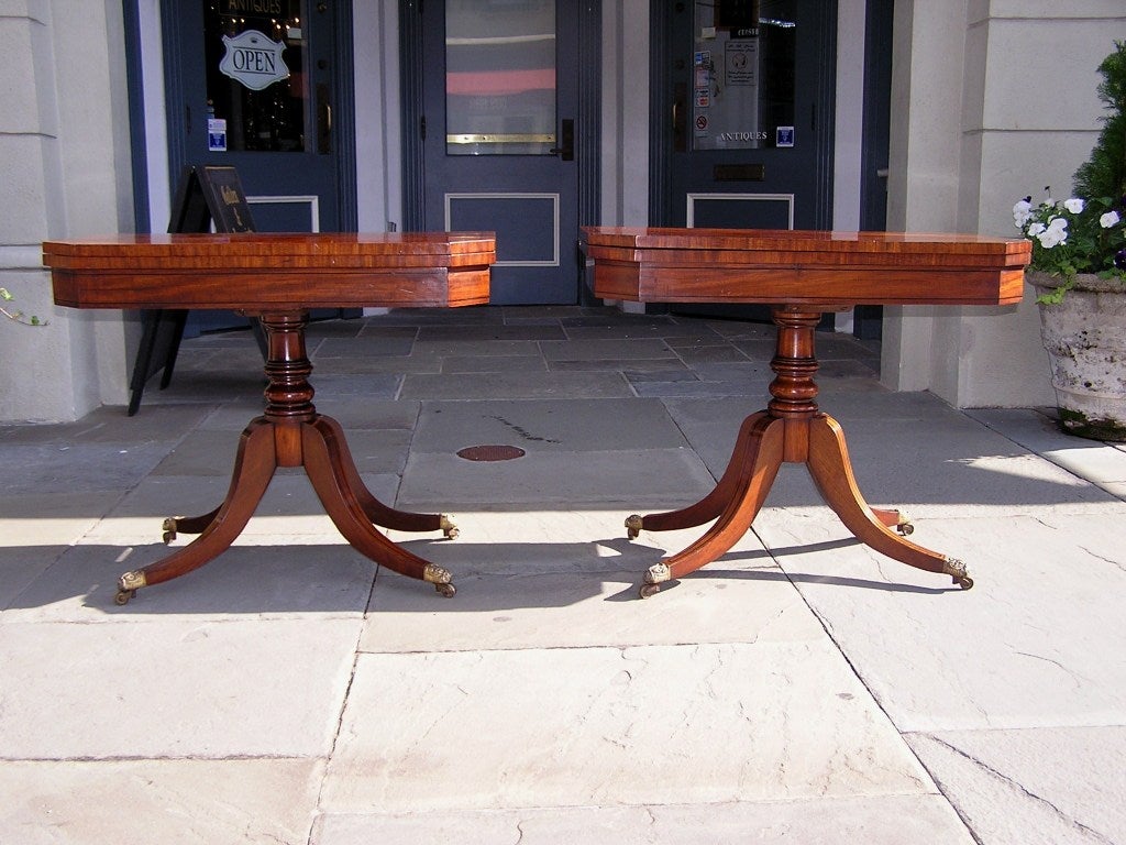 Pair of Mahogany Barbados flip top game tables with turned pedestals, ebonized string inlay, and original brass casters.