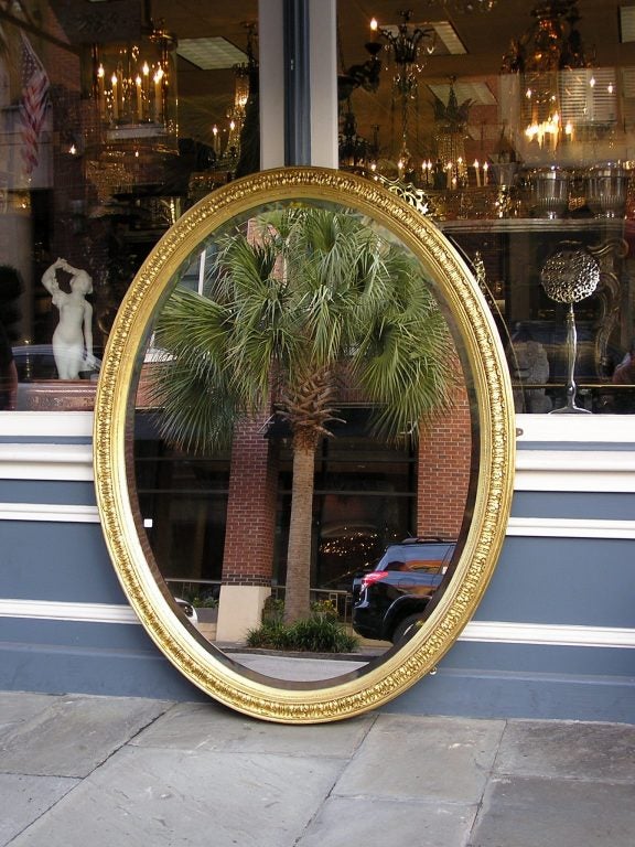 French large oval gilt wood and gesso foliage wall mirror with a carved molded edge, Interior bead work, and lambs tongue motif.  Mirror retains the original beveled glass and wood backing. Early 19th Century