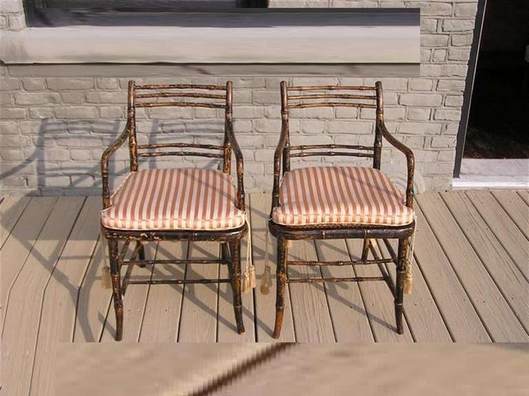 Pair of English Regency Beech painted faux bamboo arm chairs with cane seats, silk cushions, and terminating on splayed legs with stretchers.  Dealers please call for trade price.