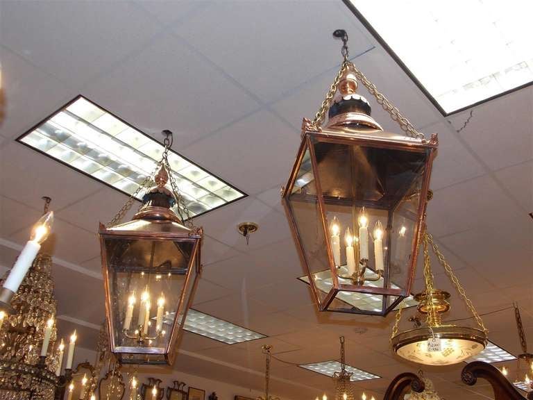 Pair of French Copper hanging lanterns with decorative finial tops, four light clusters, hinged glass doors, and ending on squared bases.  Originally gas and have been converted to electricity.  Dealers please call for trade price.