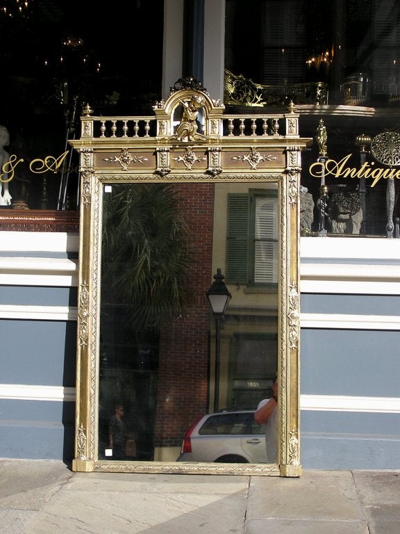 Specchio da parete francese in argento dorato e gesso a fogliame con arco centrale con cherubino che suona il flauto, gallerie laterali con terminali a urna e bordi decorativi a medaglione a fogliame. Lo specchio conserva il vetro originale e il