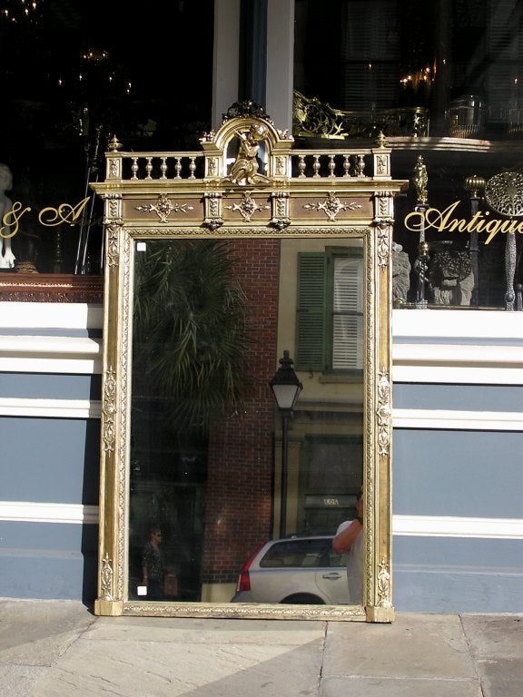 Französischer Wandspiegel aus vergoldetem Silber und Gesso mit flötendem Cherub in der Mitte, flankierenden Galerien mit Urnenknäufen und dekorativen Medailloneinfassungen. Der Spiegel behält das Originalglas und die Holzrückwand. Anfang 19.