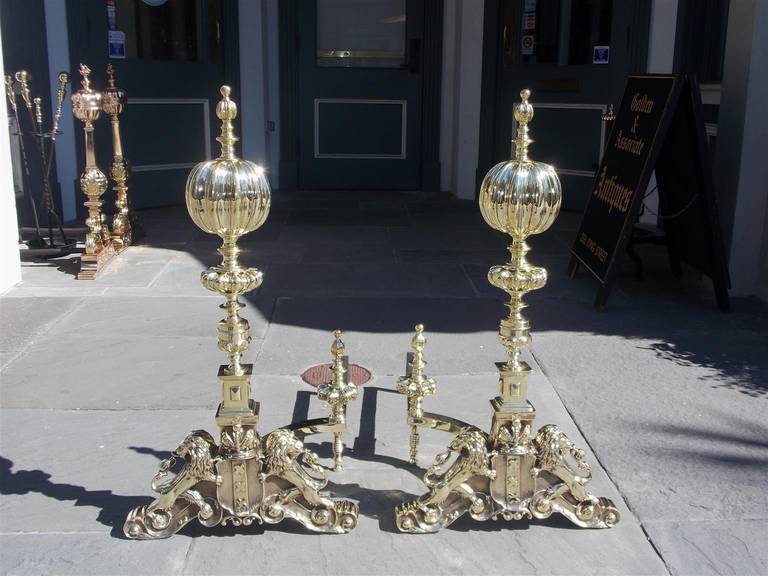 Pair of English period Regal fluted ball top andirons with turned bulbous and squared columns, matching finial log stops, and terminating on plinths with flanking lions and centered crest, Early 19th Century.
