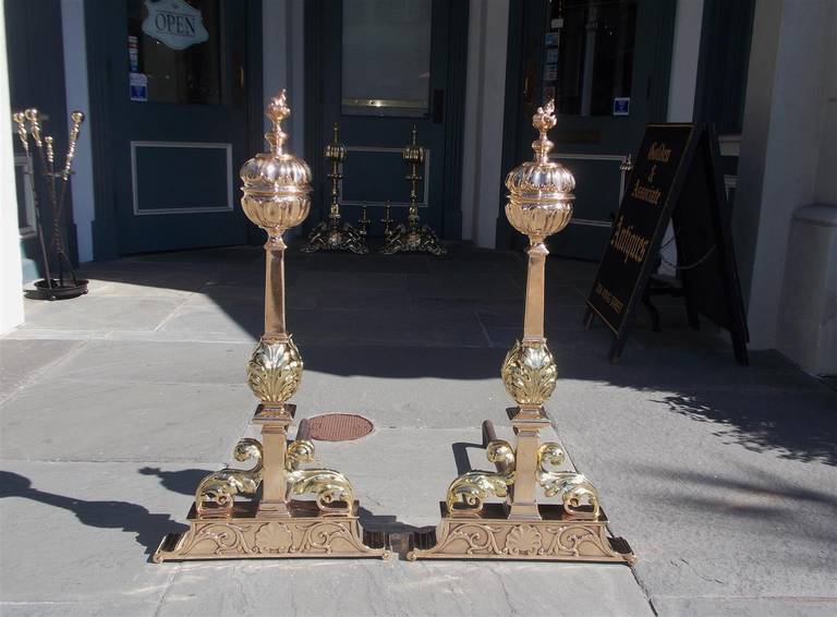 Pair of American bronze and brass andirons with flame finial tops over fluted balls, centered squared tapered columns with acanthus motif, and terminating on rectangular plinths with decorative shell and floral work. Mid 19th Century