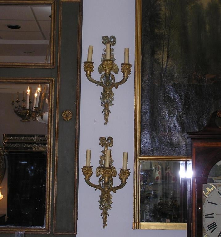 Pareja de apliques neoclásicos italianos de bronce ormolu de tres brazos con cintas decorativas flanqueantes, alas de pájaro, brazos de vela estriados con cornucopia, serpientes centrales entrelazadas con urnas estriadas y terminación con borlas