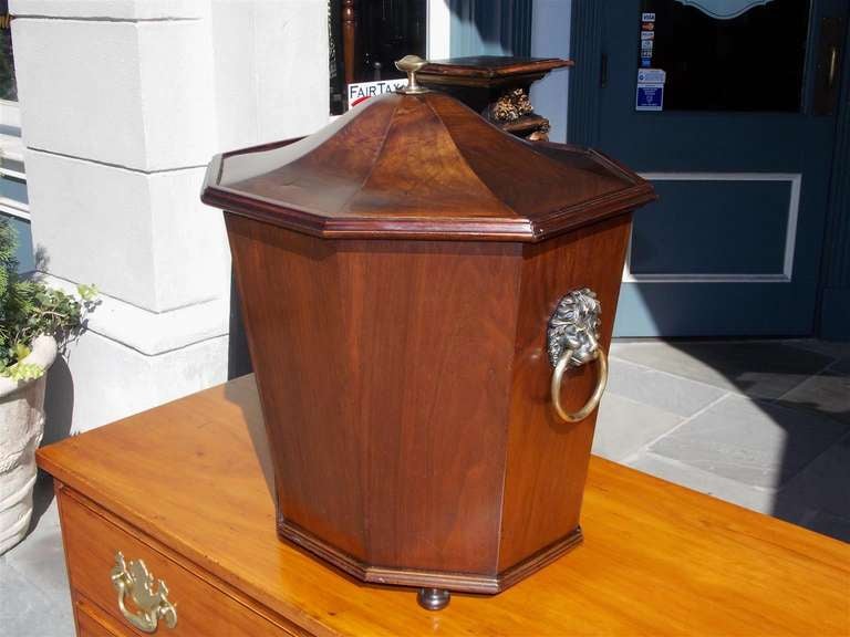 English Regency Mahogany octagon shaped wine cellarette with hinged top and brass finial, brass lions head side handles, removable original Tin insert, and terminating on bun feet.  Circa 1790