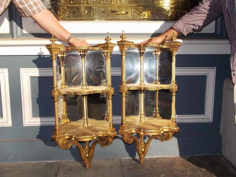 Pair of Italian gilt carved wood three tiered corner hanging wall brackets with flanking urn finials and decorative scrolled foliage motif.  Wall Brackets retain the original silvered mirrors and wood backing. Early 19th Century