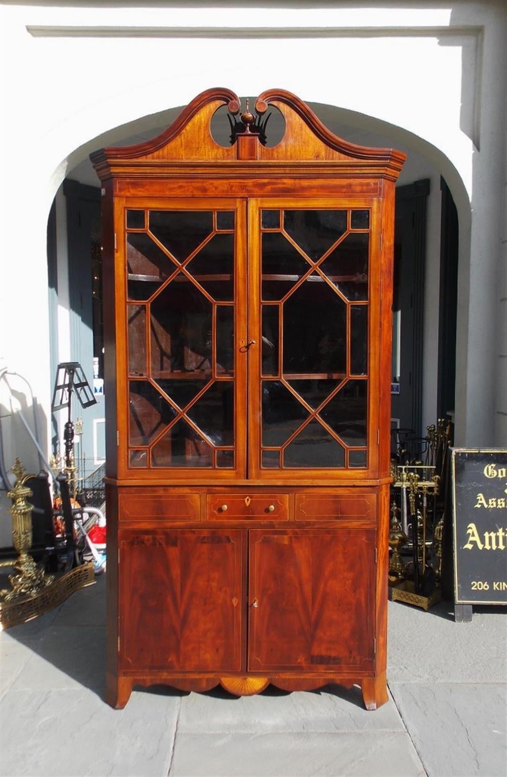 Elegante armario esquinero de caoba americana con frontón central en forma de urna con incrustaciones, puertas superiores originales con bisagras de cristal, estantería interior en forma de mariposa, un solo cajón centrado, tiradores originales de