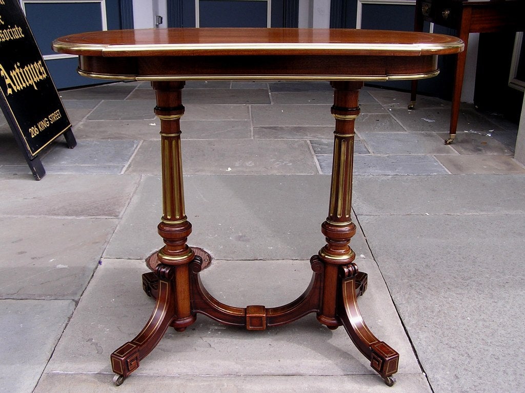 English Regency mahogany serving table with brass molded edge, brass string inlay, brass fluted columns, and terminating on scrolled legs with original brass casters.